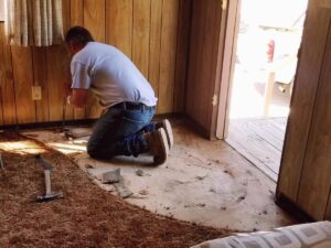 Skilled tradesperson removing old carpet in sunlit living room, preparing for new flooring.